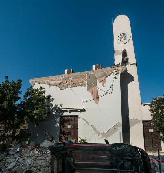 Vista d’insieme della chiesa con le macerie del portico, l’auto ribaltata e il campanile sezionato da una frattura orizzontale